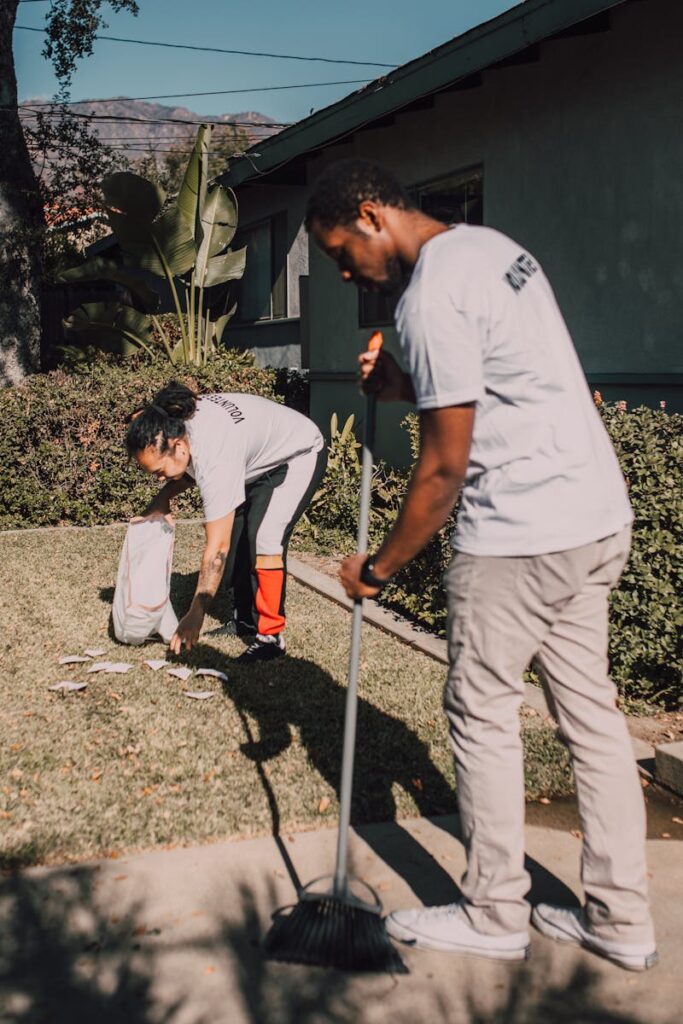 Two volunteers working together to clean a garden with a rake and collecting bags. landscaping services dubai